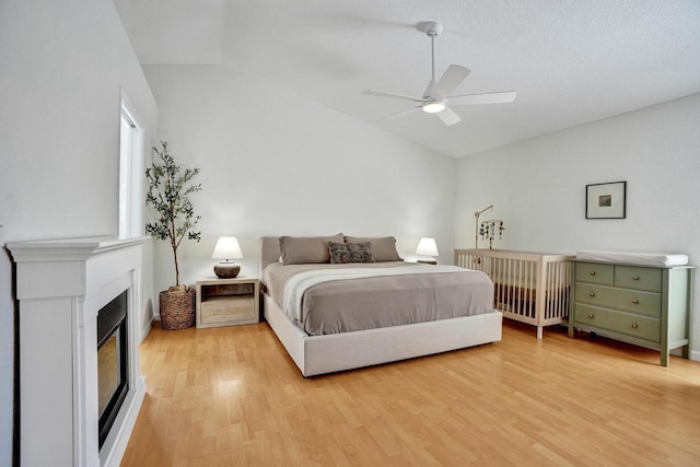 bedroom with a glass covered fireplace, light wood-style flooring, a ceiling fan, and lofted ceiling