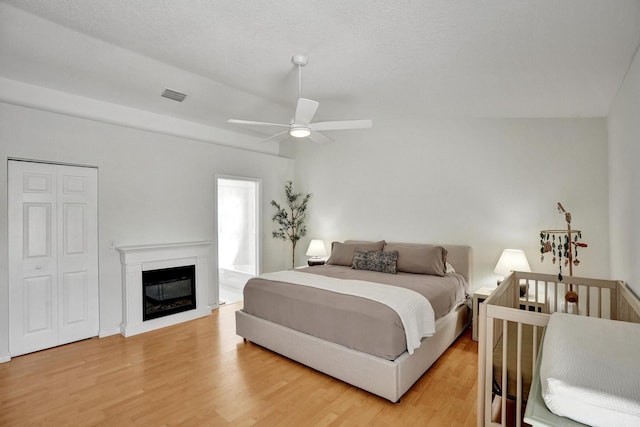 bedroom with light wood-type flooring, visible vents, a glass covered fireplace, and ceiling fan