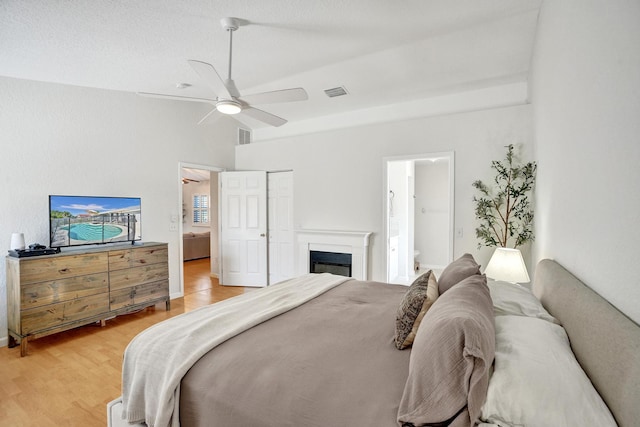 bedroom featuring a glass covered fireplace, light wood-style floors, visible vents, and ensuite bathroom