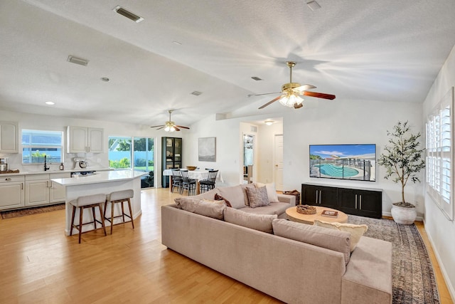 living room featuring light wood finished floors, visible vents, a textured ceiling, and lofted ceiling