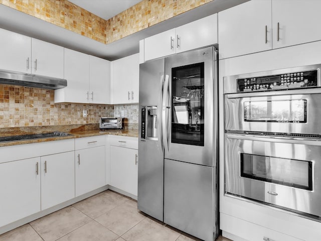 kitchen featuring under cabinet range hood, dark stone counters, decorative backsplash, stainless steel appliances, and white cabinetry