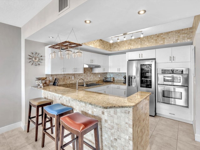 kitchen featuring under cabinet range hood, tasteful backsplash, appliances with stainless steel finishes, and a peninsula