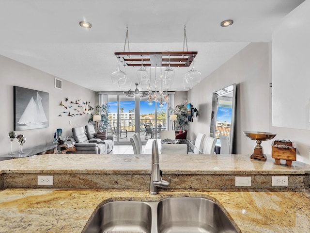 kitchen with visible vents, a sink, open floor plan, light stone countertops, and a chandelier