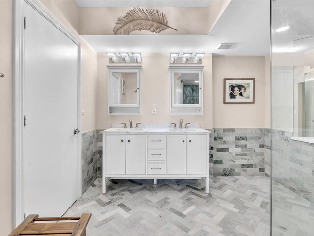 bathroom with double vanity, visible vents, tile walls, and a sink