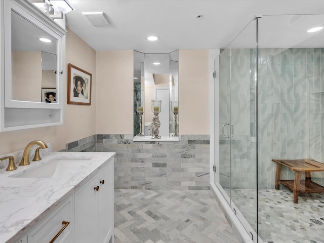 bathroom featuring visible vents, a wainscoted wall, a stall shower, tile walls, and vanity