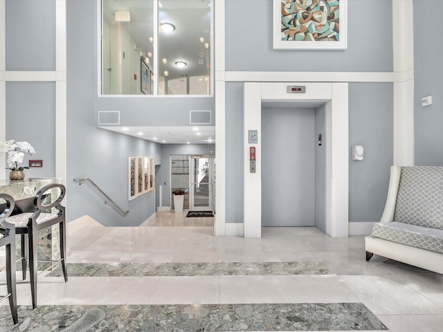 entryway with elevator, visible vents, baseboards, and a towering ceiling