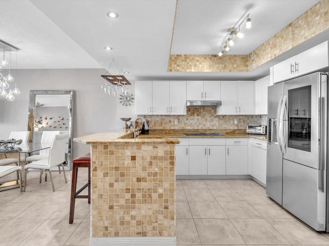 kitchen with under cabinet range hood, decorative backsplash, light tile patterned flooring, stainless steel fridge, and black electric cooktop