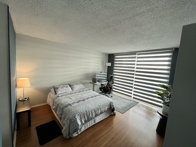 bedroom featuring floor to ceiling windows, a textured ceiling, baseboards, and wood finished floors