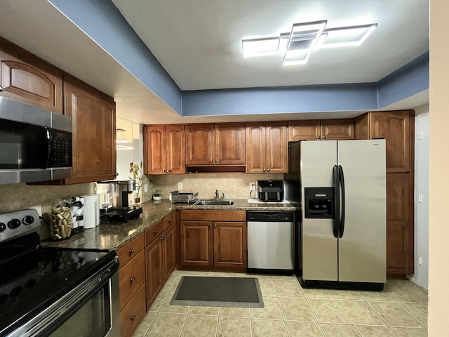 kitchen featuring light tile patterned floors, a sink, appliances with stainless steel finishes, brown cabinets, and backsplash