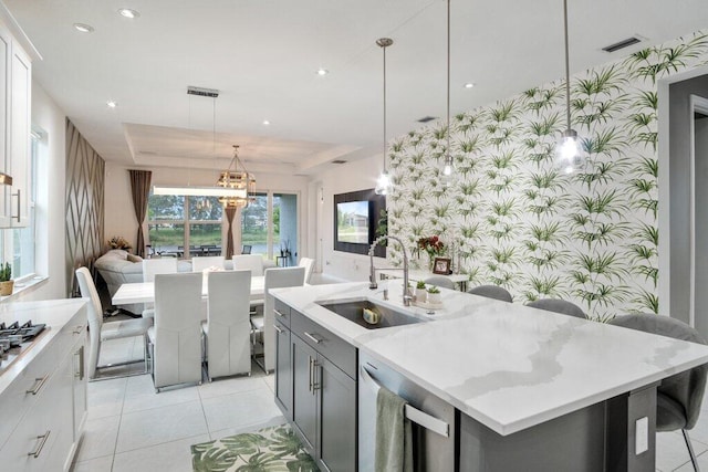 kitchen featuring wallpapered walls, visible vents, appliances with stainless steel finishes, a tray ceiling, and a sink