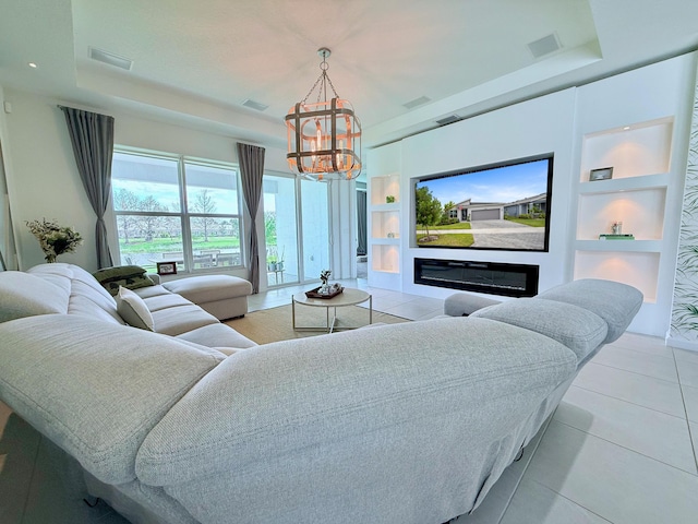 living room with built in shelves, a glass covered fireplace, a raised ceiling, and visible vents