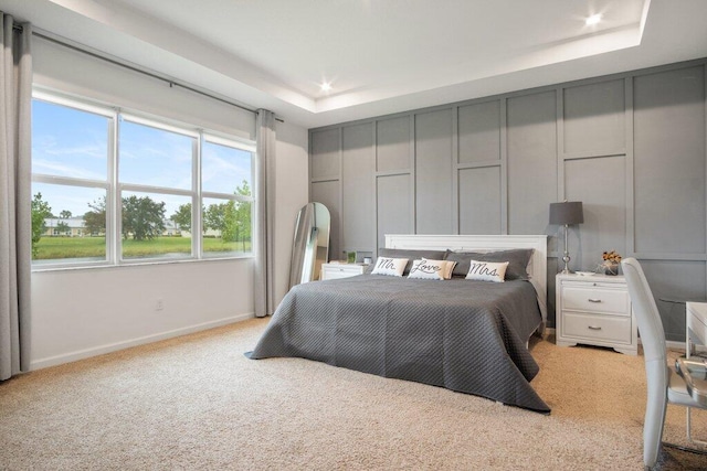 bedroom featuring baseboards, a tray ceiling, a decorative wall, and carpet flooring