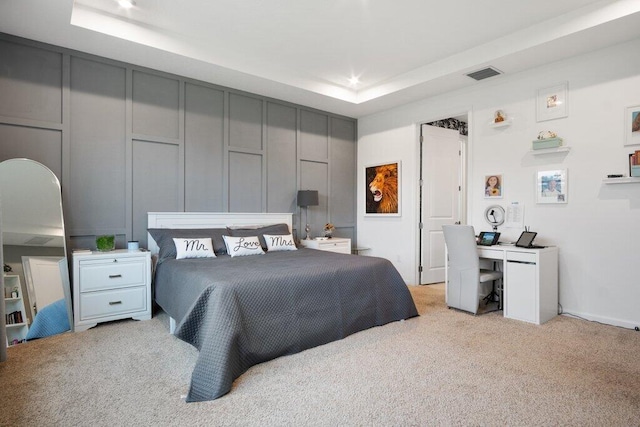 bedroom featuring light carpet, a tray ceiling, visible vents, and a decorative wall