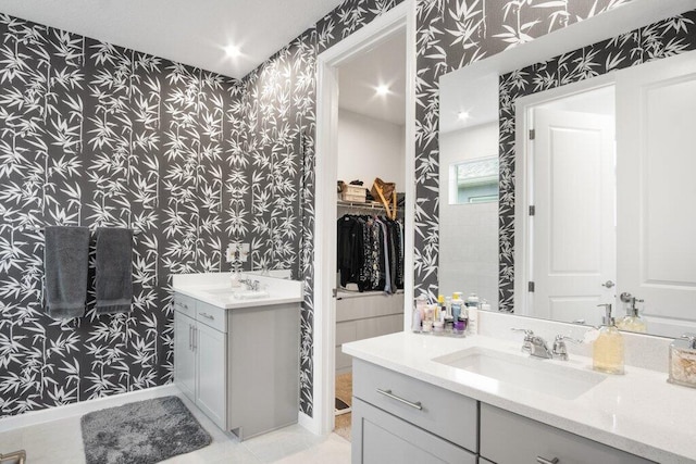 full bath featuring a walk in closet, wallpapered walls, two vanities, and a sink