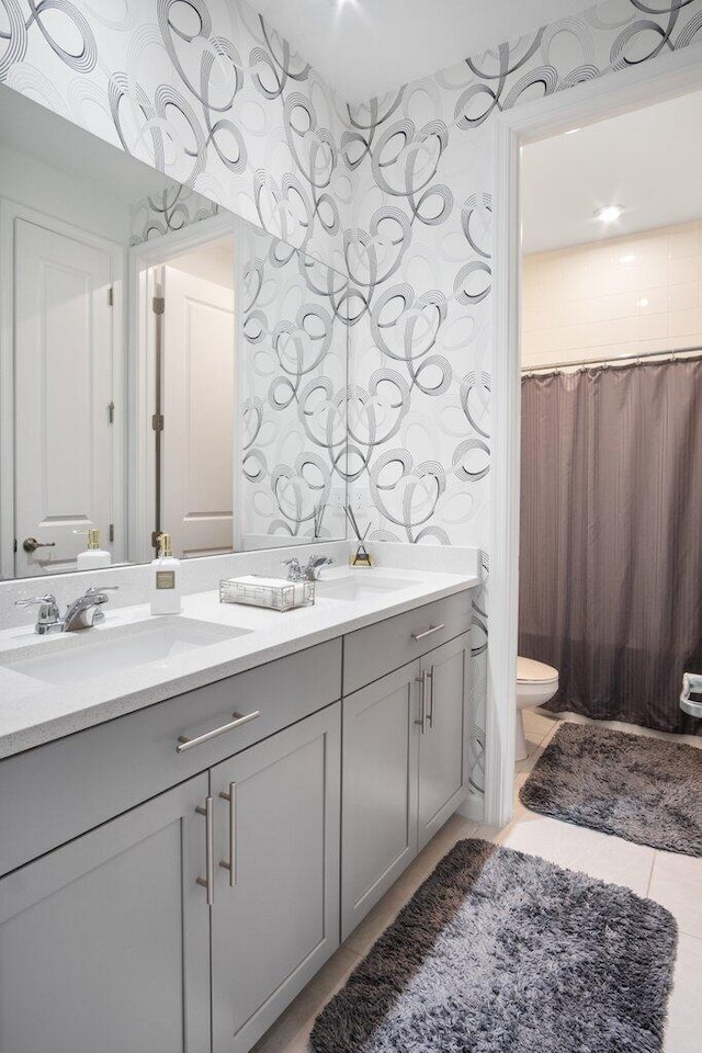 bathroom featuring double vanity, a sink, toilet, and wallpapered walls