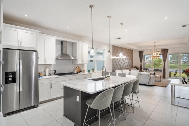 kitchen featuring light tile patterned flooring, a sink, gas stovetop, wall chimney range hood, and stainless steel refrigerator with ice dispenser