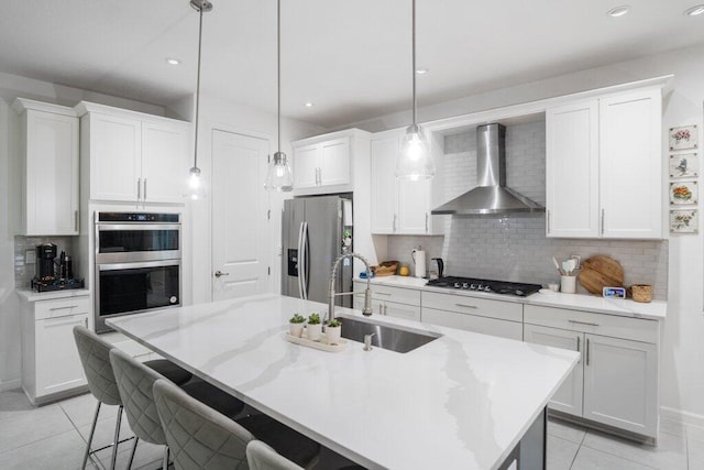 kitchen featuring appliances with stainless steel finishes, white cabinetry, a sink, and wall chimney exhaust hood