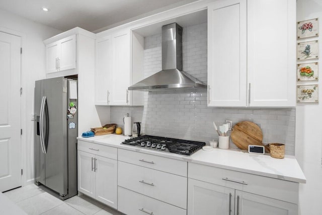 kitchen featuring light tile patterned floors, stainless steel appliances, decorative backsplash, white cabinetry, and wall chimney range hood