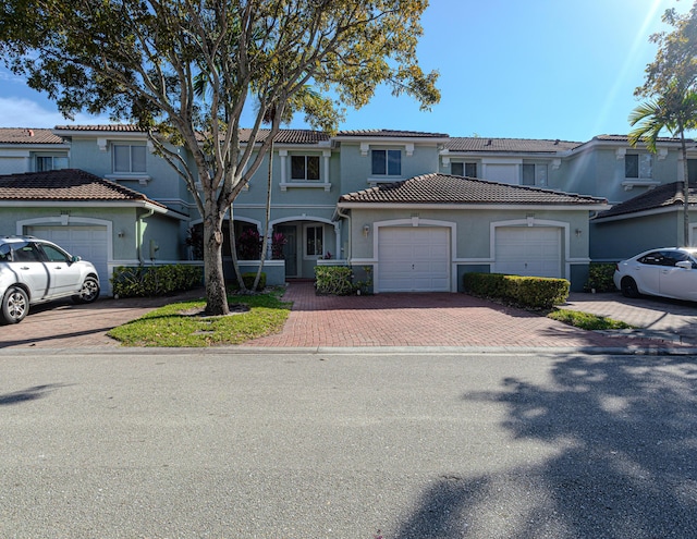 multi unit property featuring stucco siding, an attached garage, a tile roof, and decorative driveway