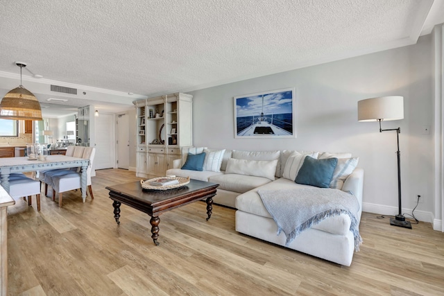 living room with ornamental molding, visible vents, light wood-style flooring, and a textured ceiling