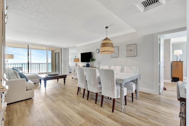 dining room featuring light wood-style floors, visible vents, a textured ceiling, and baseboards