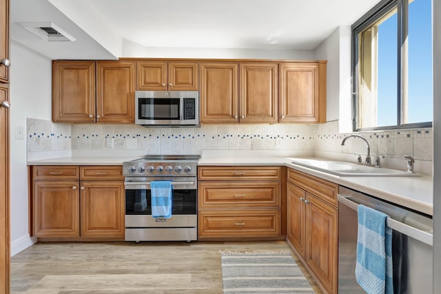 kitchen with appliances with stainless steel finishes, brown cabinetry, and a sink