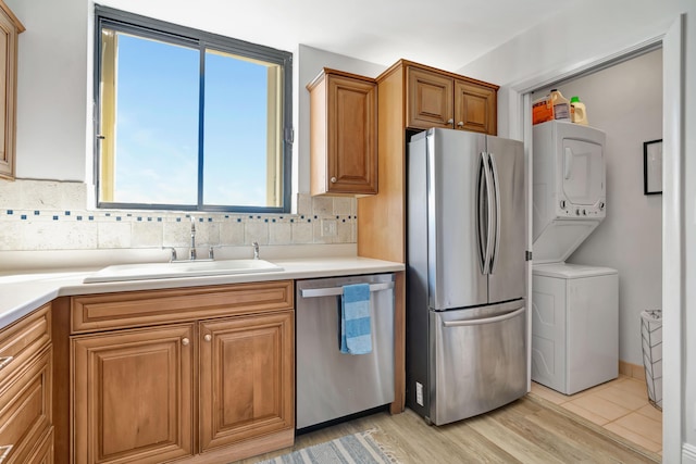 kitchen featuring stacked washer and clothes dryer, light countertops, backsplash, appliances with stainless steel finishes, and a sink