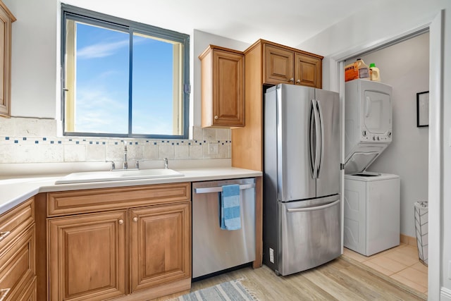 kitchen featuring stainless steel appliances, stacked washer / drying machine, tasteful backsplash, light countertops, and a sink