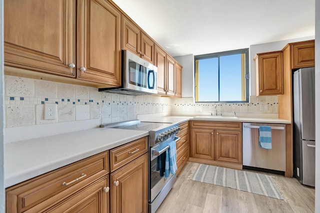 kitchen with brown cabinets, light wood-style floors, stainless steel appliances, and a sink