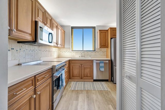 kitchen featuring appliances with stainless steel finishes, a sink, light countertops, light wood-type flooring, and backsplash