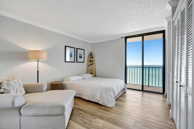 bedroom with a textured ceiling, light wood-style floors, access to outside, floor to ceiling windows, and crown molding