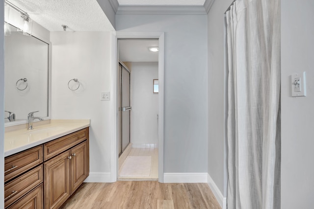 full bathroom featuring wood finished floors, vanity, baseboards, ornamental molding, and a stall shower