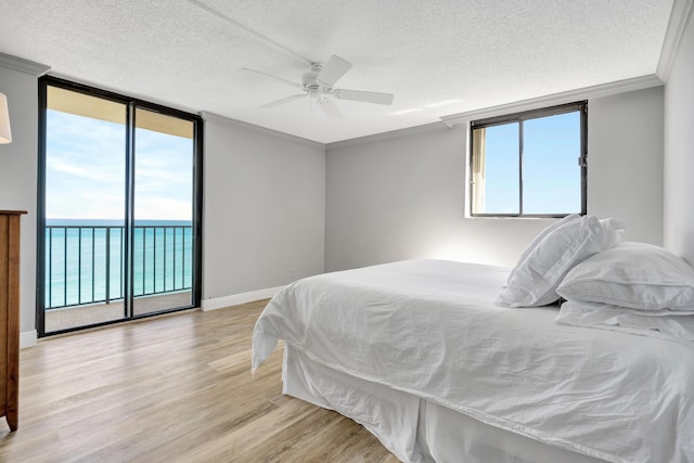 bedroom featuring access to exterior, light wood finished floors, ornamental molding, a wall of windows, and baseboards