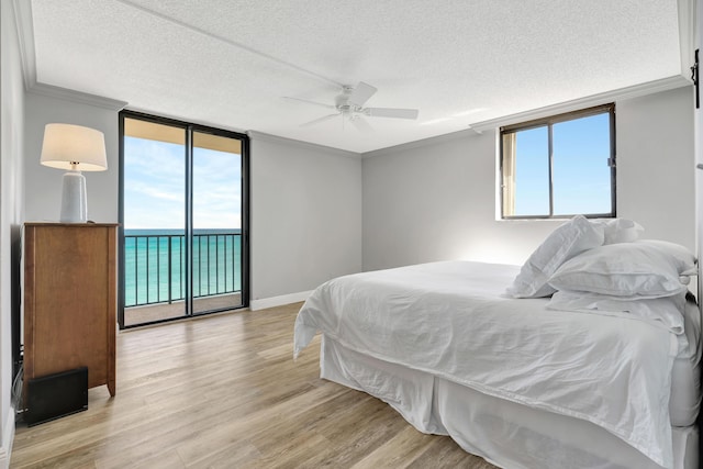 bedroom with floor to ceiling windows, crown molding, light wood-style flooring, a textured ceiling, and access to outside