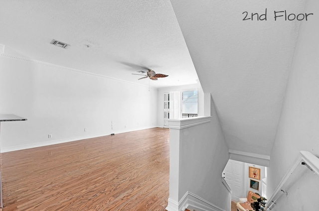 unfurnished living room with visible vents, a textured ceiling, wood finished floors, baseboards, and ceiling fan