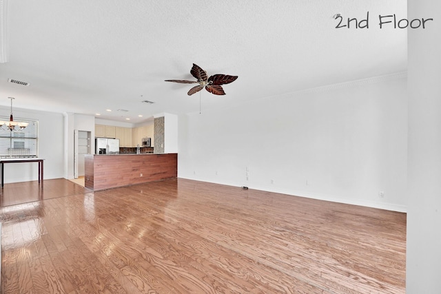 unfurnished living room featuring visible vents, ceiling fan with notable chandelier, light wood-type flooring, and baseboards