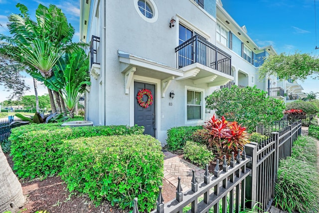 doorway to property featuring stucco siding, a balcony, and fence