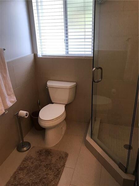 bathroom with toilet, a stall shower, tile patterned flooring, and tile walls