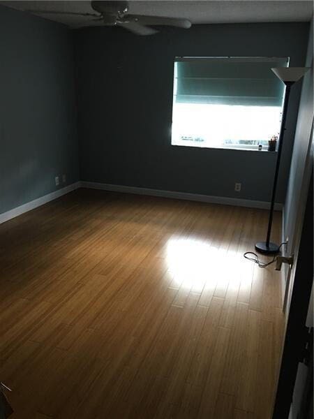 unfurnished room featuring ceiling fan, wood finished floors, and baseboards