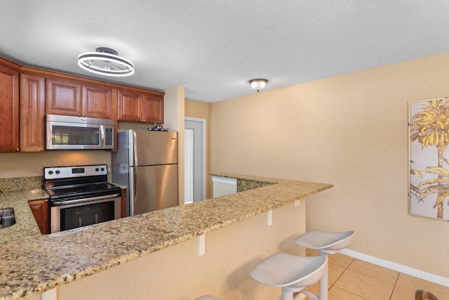 kitchen featuring light stone counters, light tile patterned floors, baseboards, a breakfast bar, and stainless steel appliances