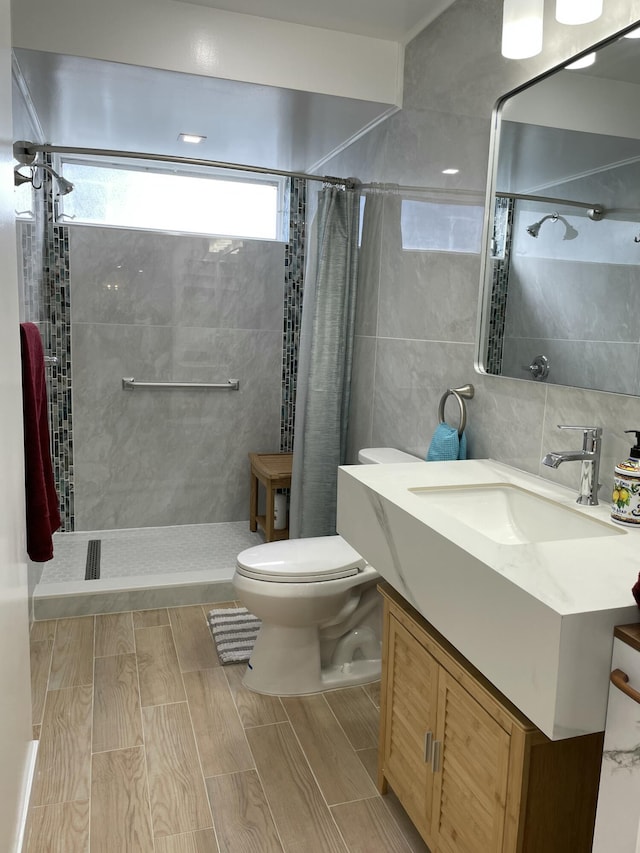 full bathroom featuring tiled shower, vanity, toilet, and tile walls