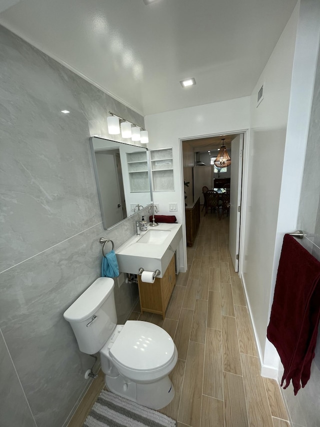 bathroom with wood finish floors, visible vents, toilet, and tile walls