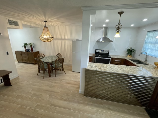 kitchen featuring visible vents, wall chimney range hood, freestanding refrigerator, electric range, and a sink