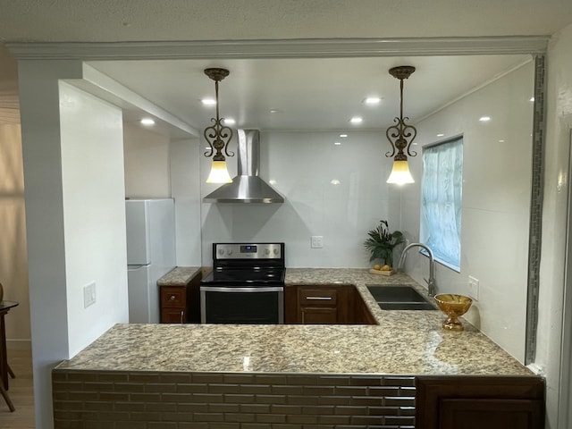 kitchen with a sink, stainless steel electric stove, freestanding refrigerator, wall chimney range hood, and light stone countertops