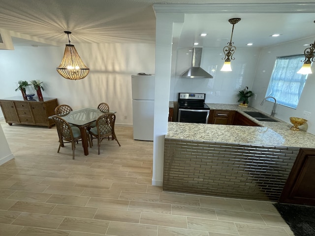 kitchen featuring wall chimney range hood, stainless steel electric range oven, light stone counters, freestanding refrigerator, and a sink