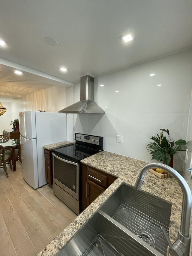 kitchen featuring light stone counters, electric range, freestanding refrigerator, light wood-style floors, and wall chimney exhaust hood