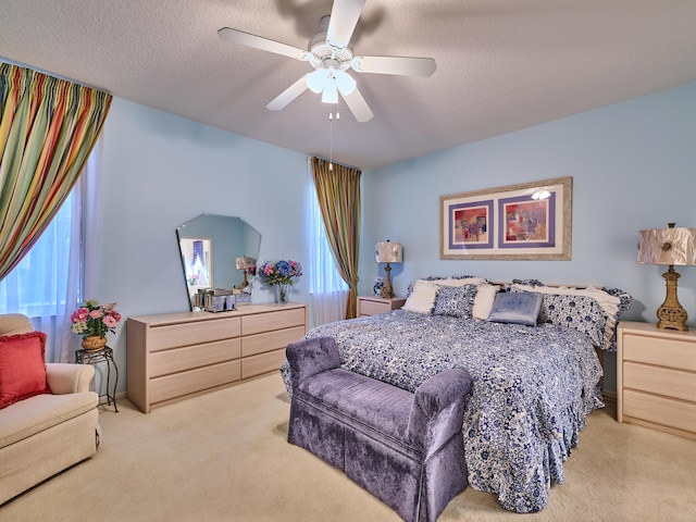 bedroom with a ceiling fan, light colored carpet, and a textured ceiling