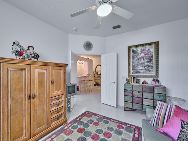 interior space featuring a textured ceiling, light tile patterned flooring, visible vents, and a ceiling fan