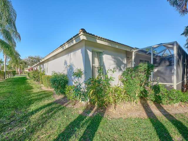 view of side of property with a lanai, a yard, a tiled roof, and stucco siding