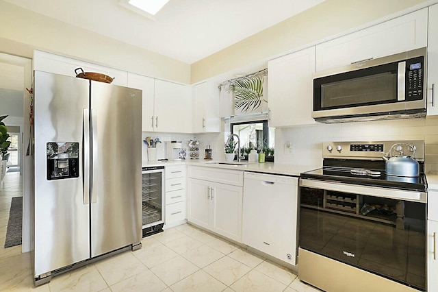 kitchen with wine cooler, a sink, light countertops, appliances with stainless steel finishes, and decorative backsplash